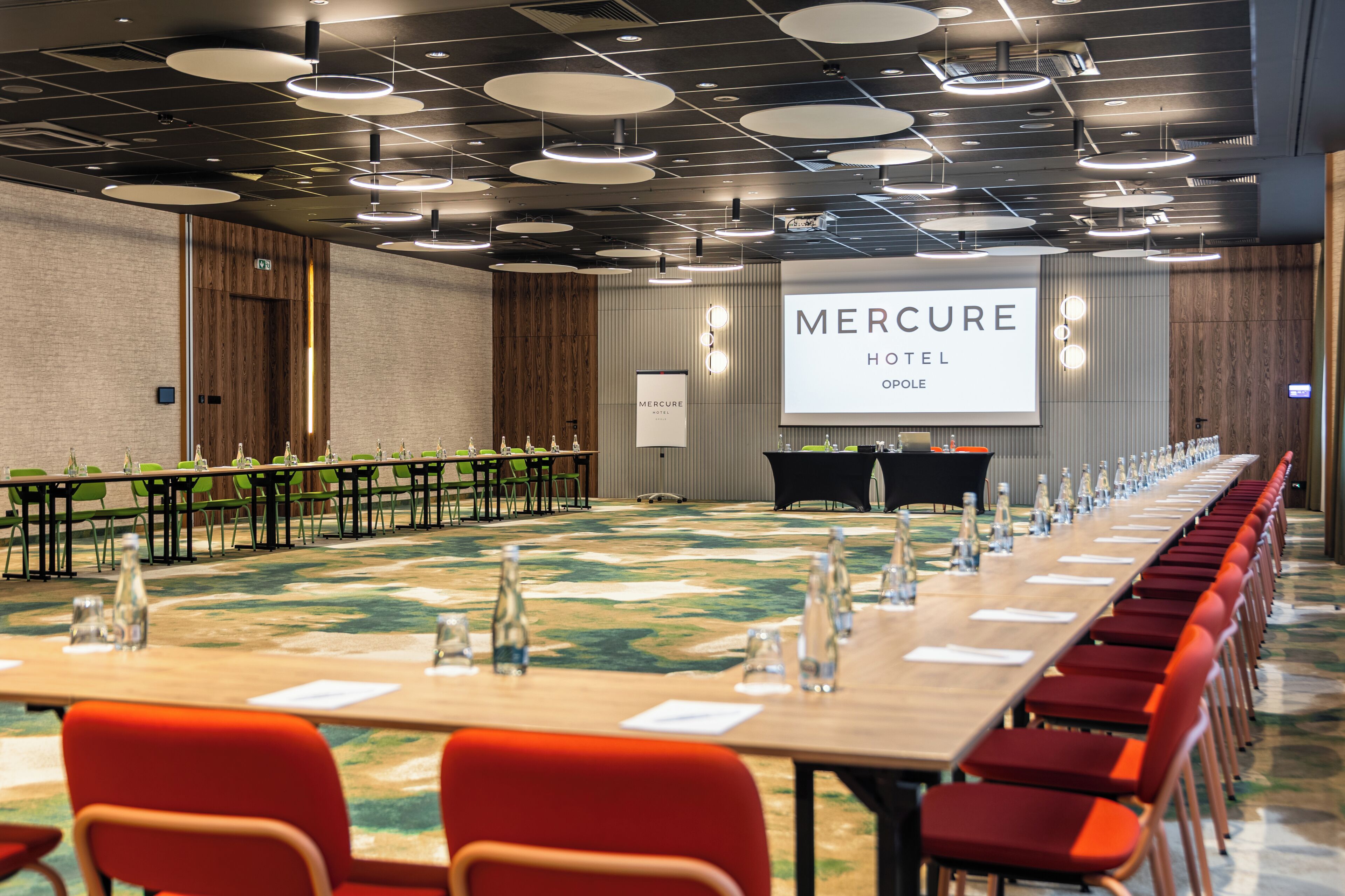 Une salle de conférence avec une longue table, des chaises et un écran affichant le nom « Hôtel Mercure ».