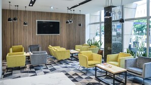 Un vestíbulo moderno con asientos de color amarillo y gris, una gran pantalla de televisión y un mostrador de recepción.