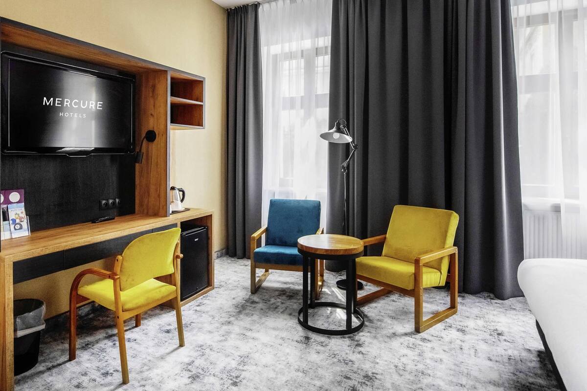 Habitación de hotel con televisión de pantalla plana, un escritorio con cafetera, dos sillones, una mesita redonda y una cama.