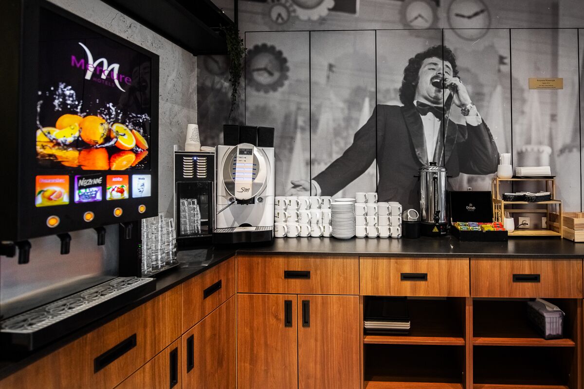 A hotel bar area with a digital screen displaying fruit juices, a coffee machine, and a coffee station.