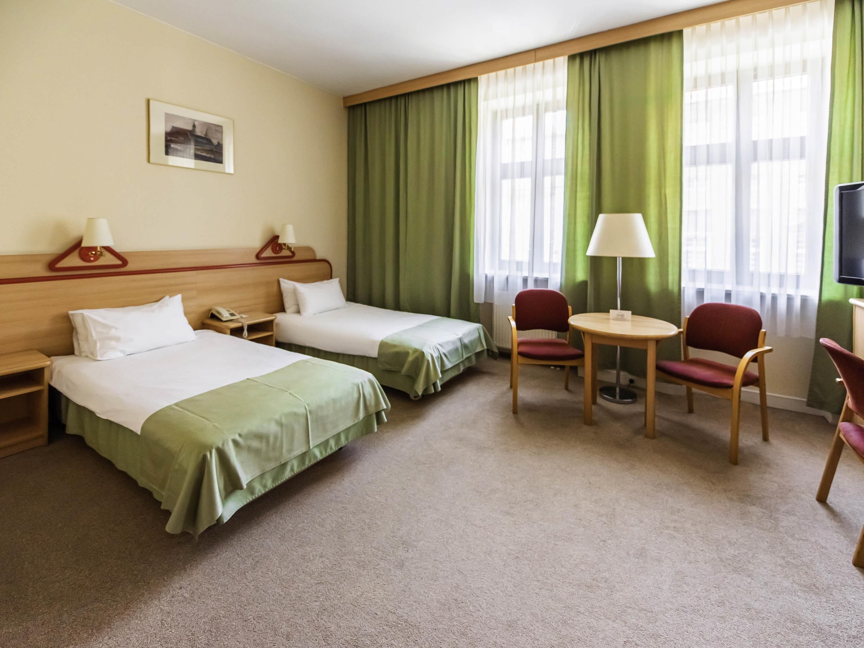 Una habitación de hotel con dos camas, un escritorio, una silla, un televisor y una ventana con cortinas.
