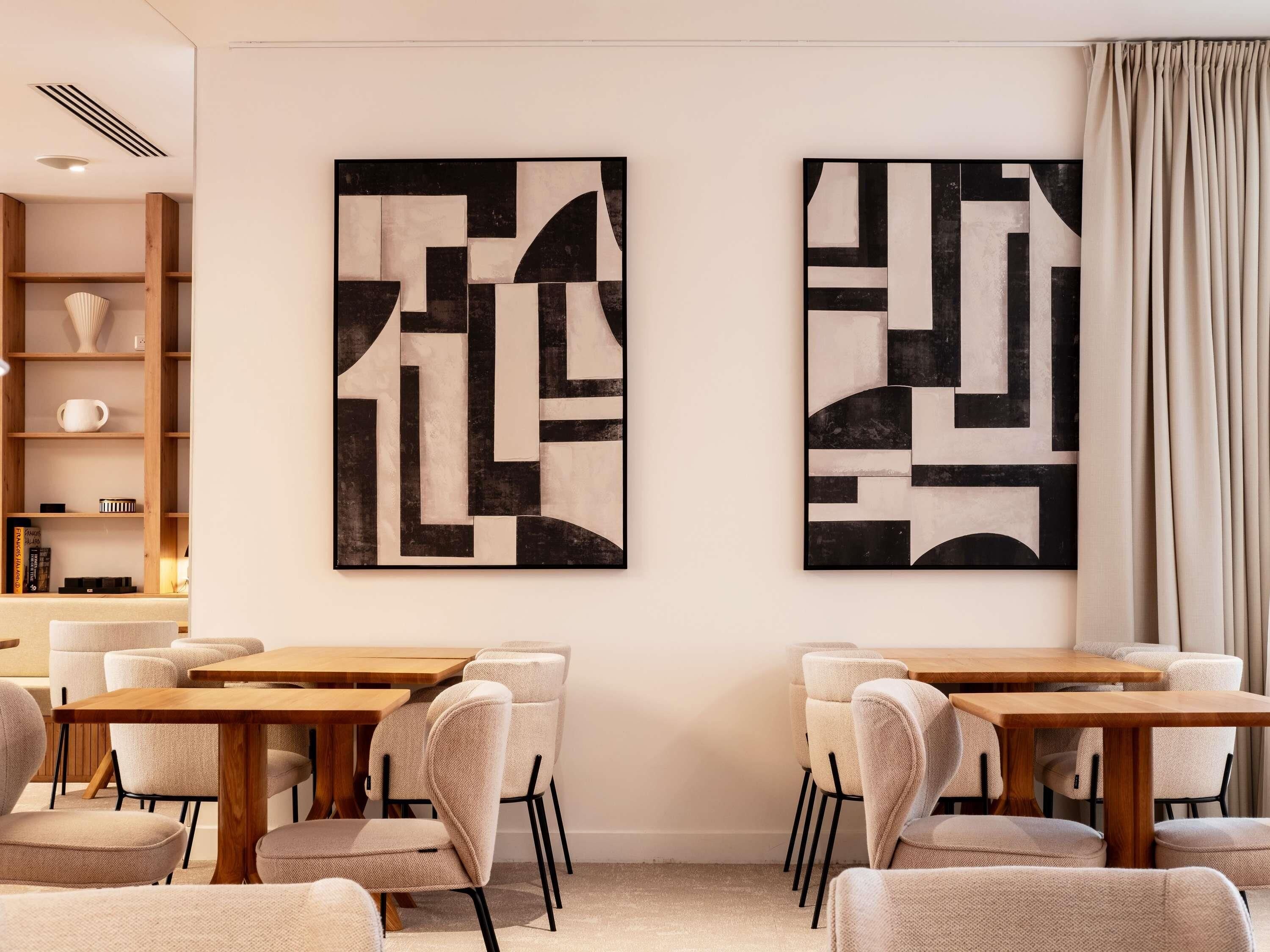 Un espace repas moderne avec une table et des chaises en bois, deux tableaux abstraits accrochés au mur et une bibliothèque agrémentée d’objets décoratifs.