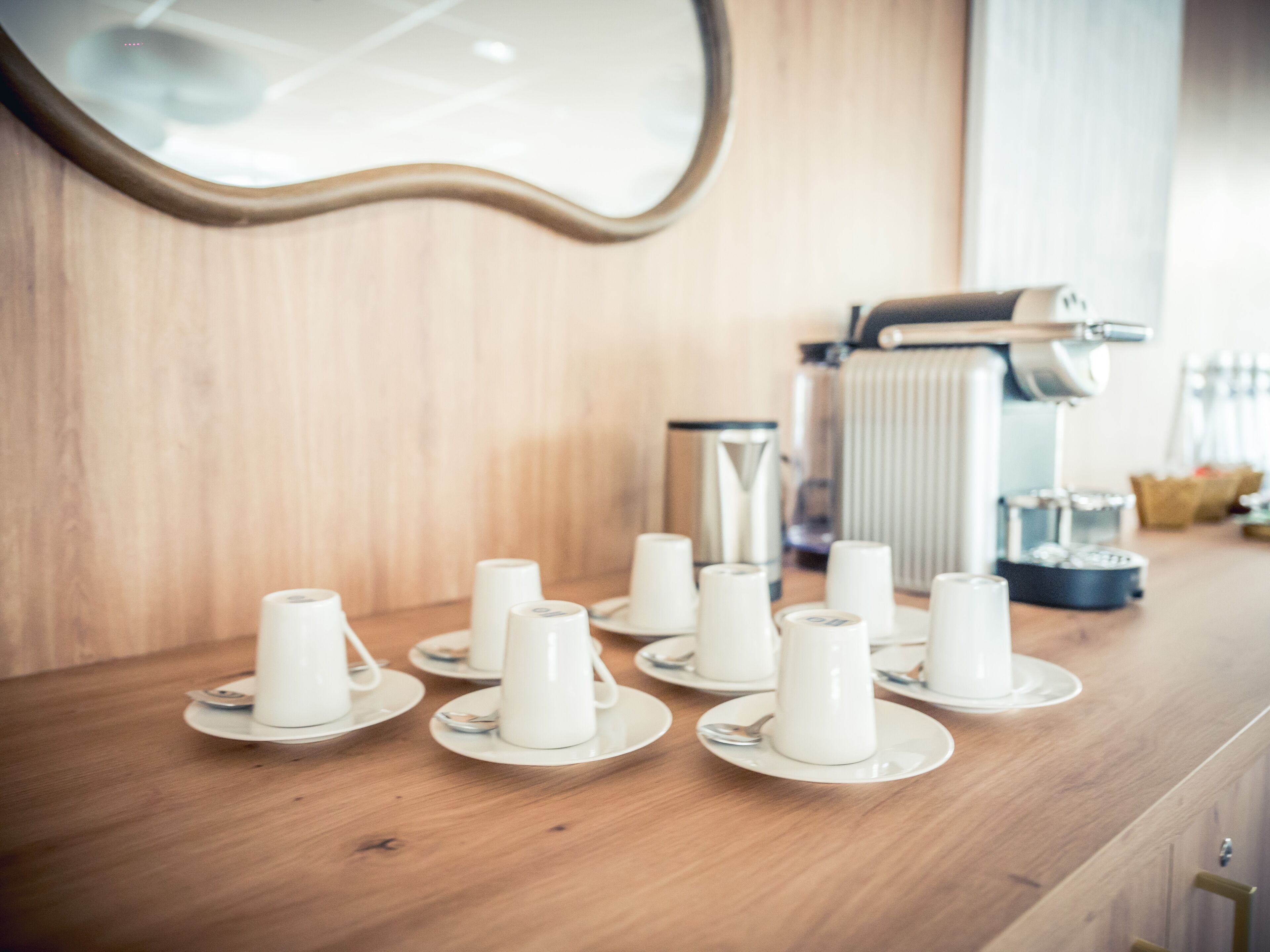 Une table en bois, avec des tasses et des soucoupes blanches, une bouilloire et une machine à café.