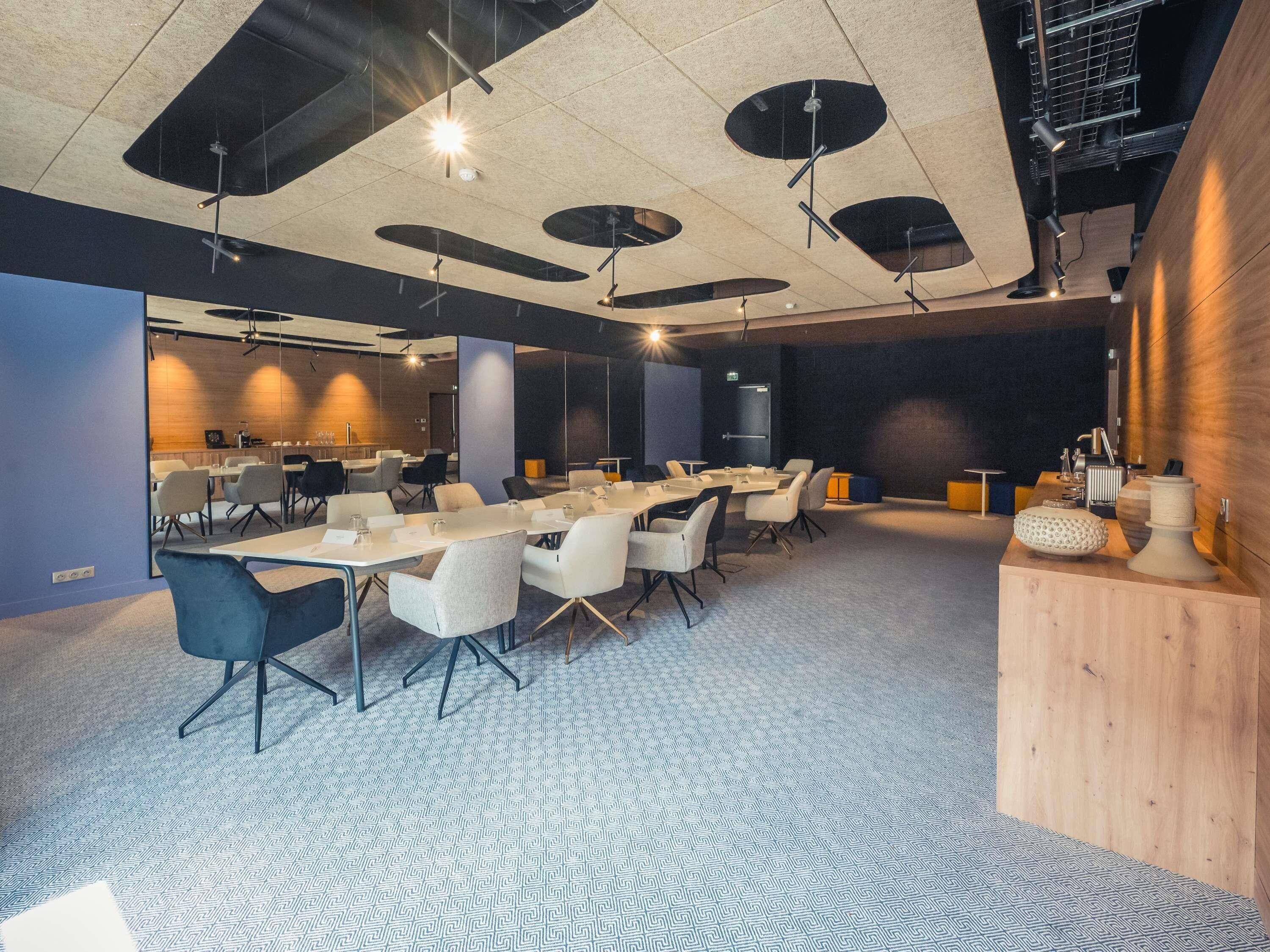 A conference room with tables and chairs, a wooden accent wall, and a patterned carpet.