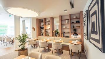 Un comedor moderno con mesas y sillas redondas, estanterías de madera con objetos decorativos y un cuadro abstracto grande en la pared.