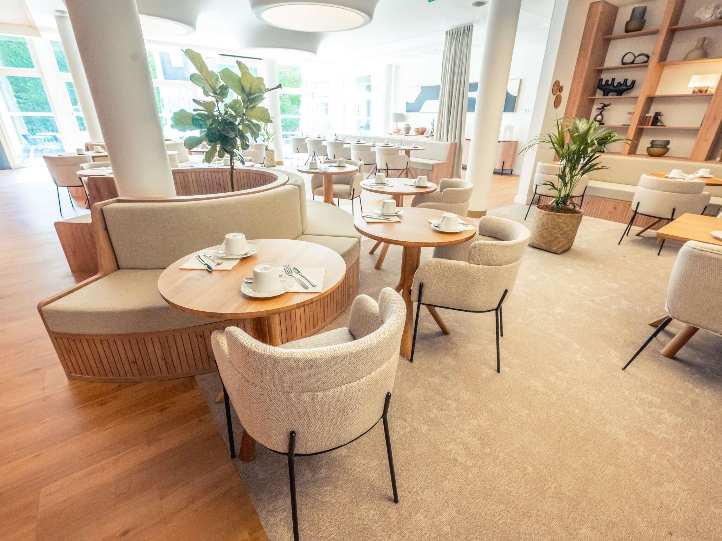 Eine moderne Hotellobby mit runden Tischen, bequemen Sitzgelegenheiten und großen Fenstern.
