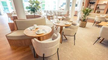 Eine moderne Hotellobby mit runden Tischen, bequemen Sitzgelegenheiten und großen Fenstern.