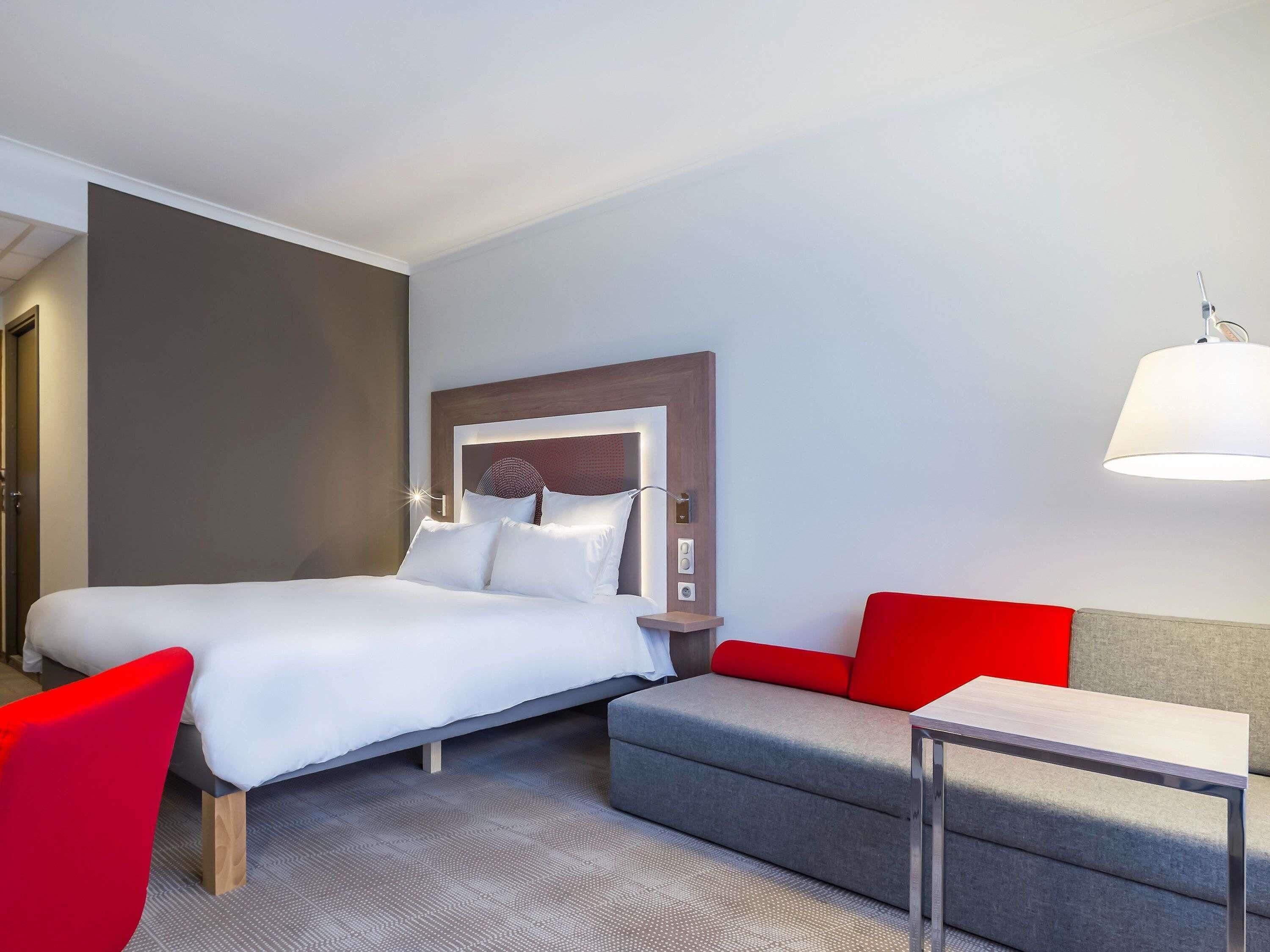 A hotel room with a bed, a desk, a chair, and a sofa.