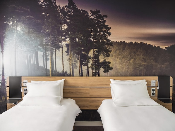 A double bed with white linens, a wooden headboard, and two bedside tables with speakers.