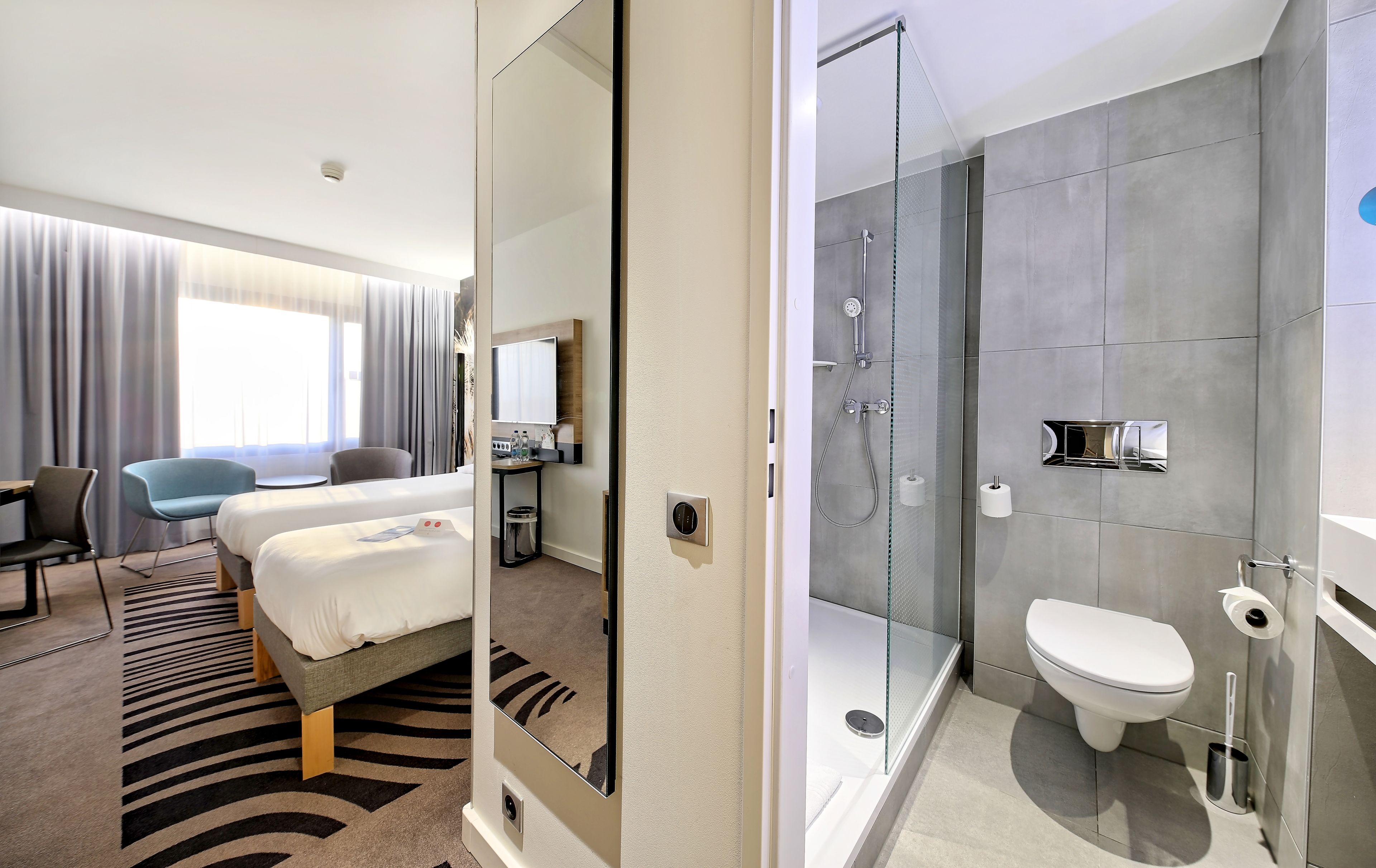 Habitación de hotel con cama, escritorio, silla y baño privado con ducha, inodoro y lavamanos.