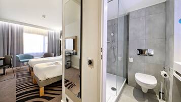 Habitación de hotel con cama, escritorio, silla y baño privado con ducha, inodoro y lavamanos.
