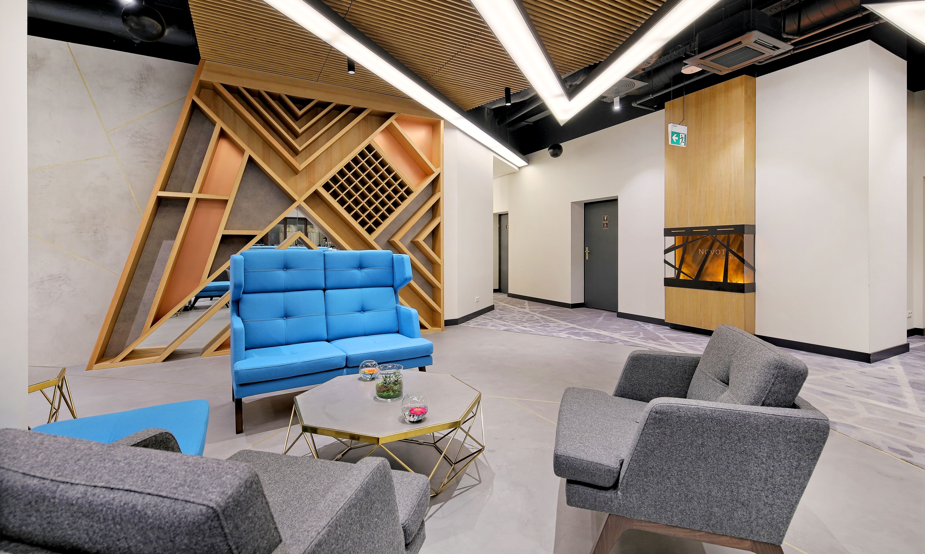 Un espace détente moderne avec un canapé bleu, des fauteuils gris et une petite table ronde agrémentée d’objets décoratifs.