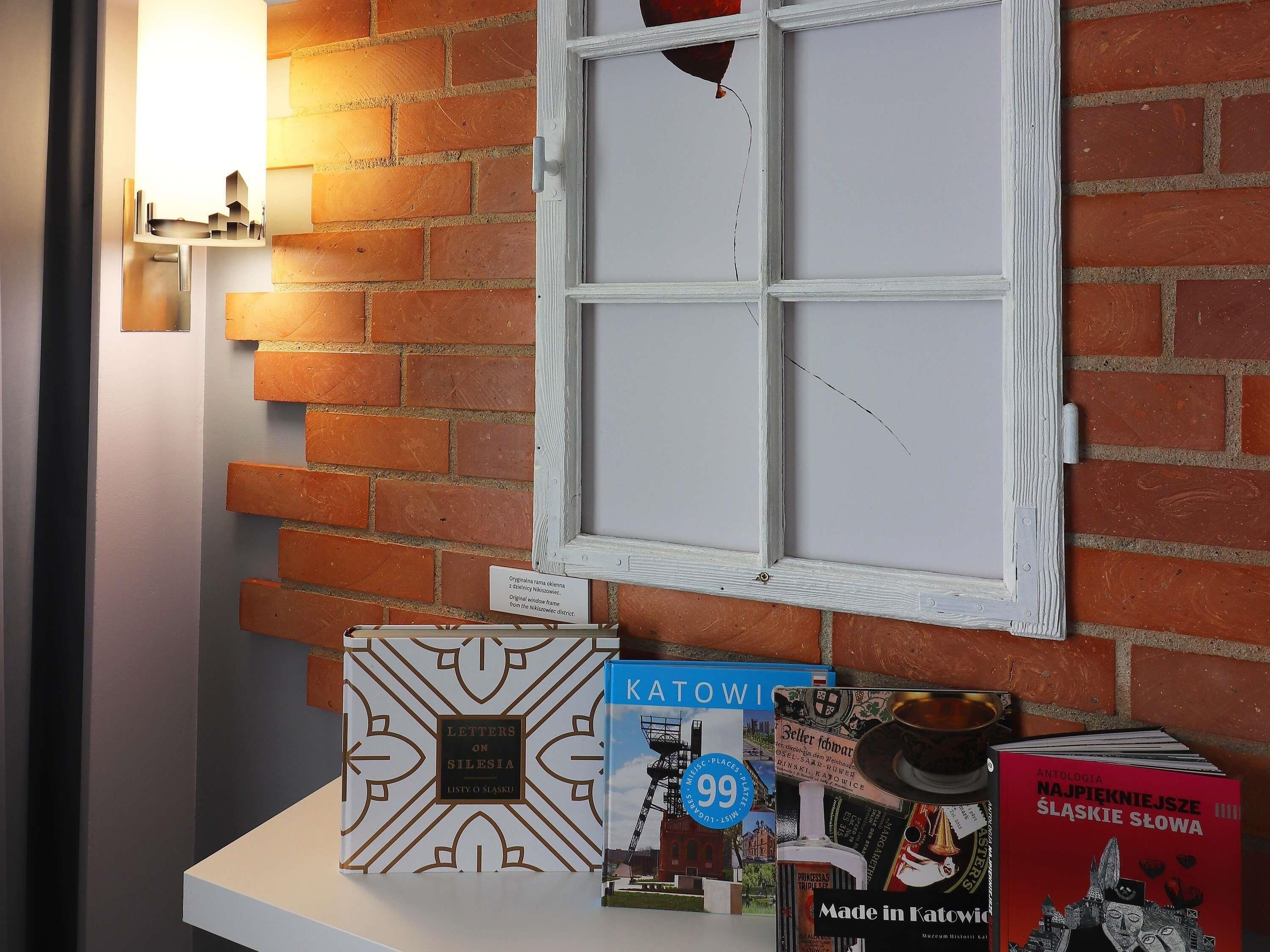 A room with a brick wall, a window with a broken pane, and a display of books.