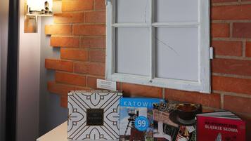 A room with a brick wall, a window with a broken pane, and a display of books.
