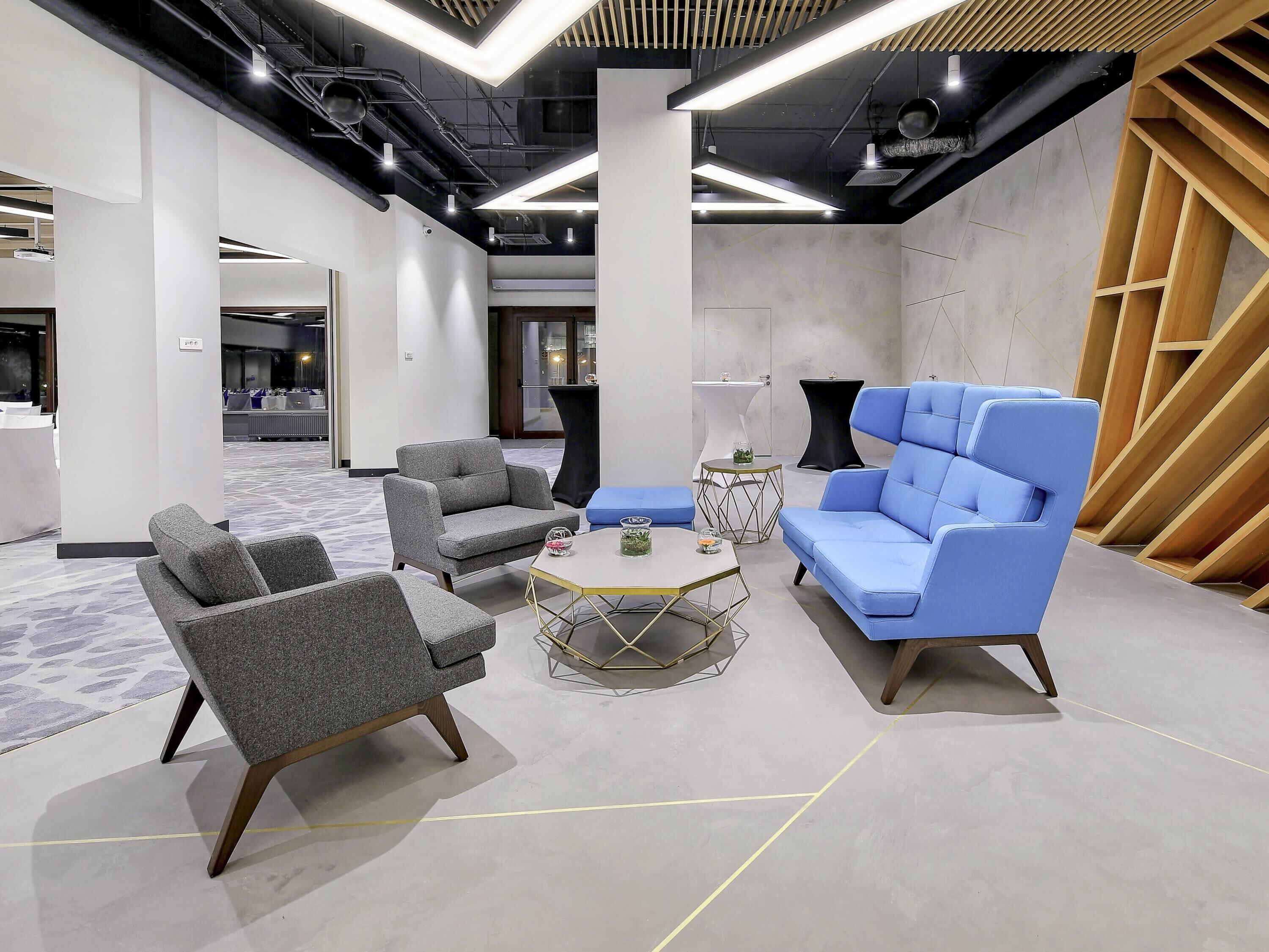 A modern lounge area with grey and blue seating, a round coffee table, and a geometric wall design.