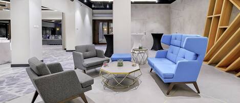 A modern lounge area with grey and blue seating, a round coffee table, and a geometric wall design.