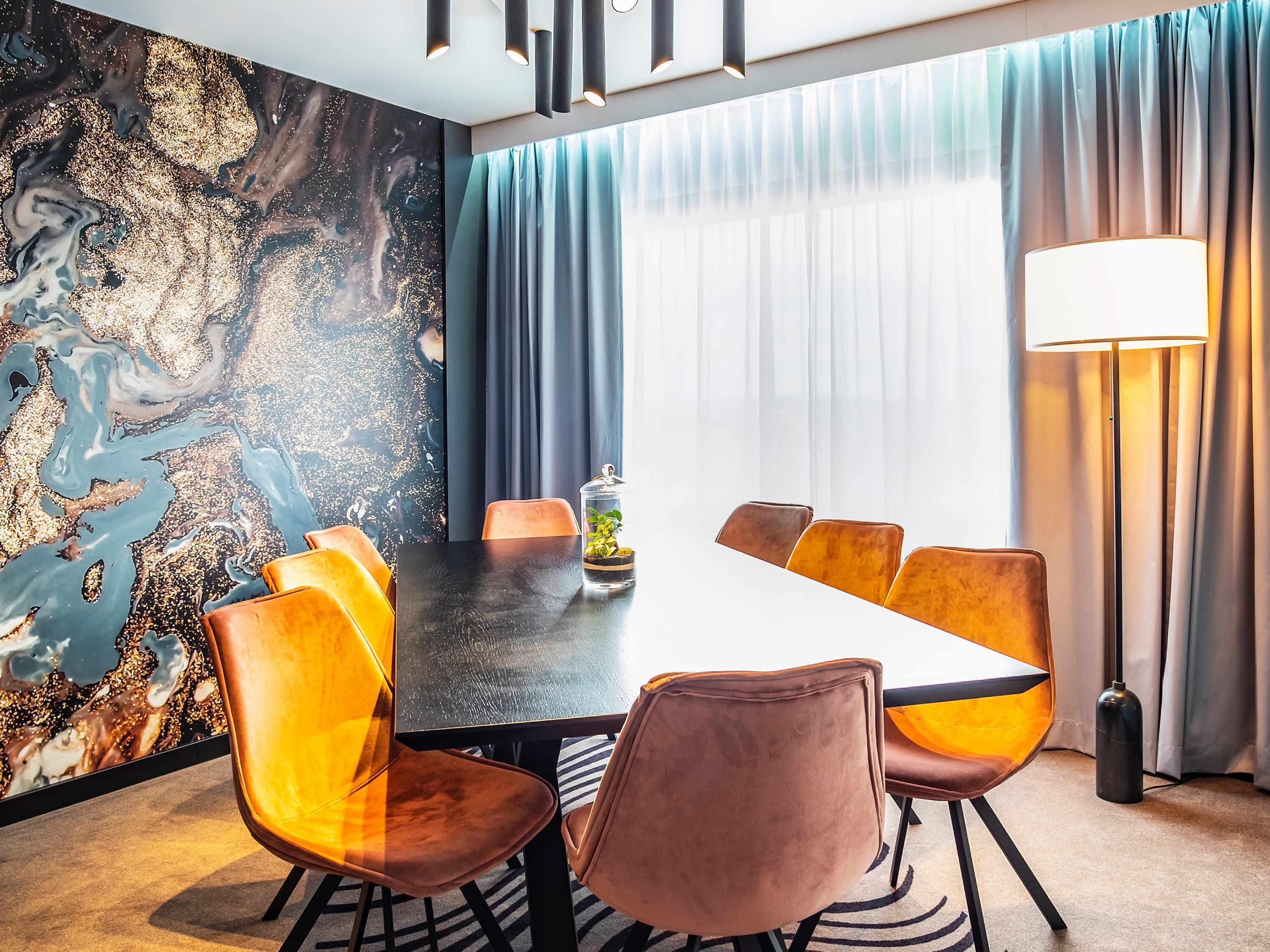 A modern dining room with a black table, velvet chairs, a decorative wall, and a large window with curtains.
