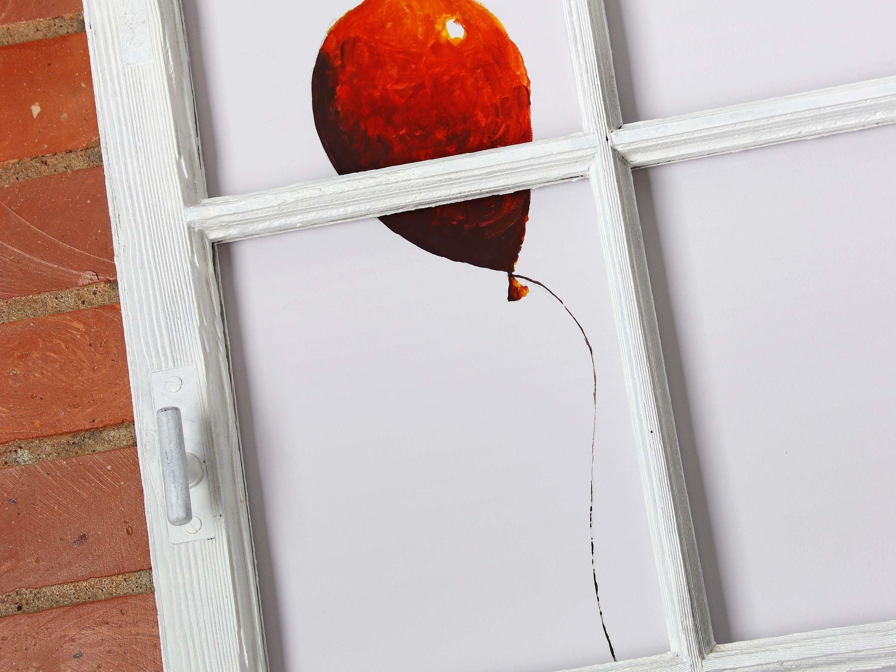 Janela com moldura branca e um balão vermelho amarrado no parapeito.