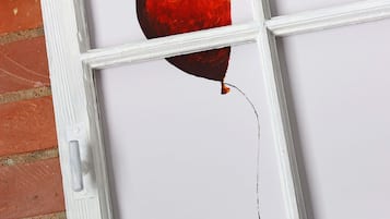 A window with a white frame and a red balloon tied to the sill.
