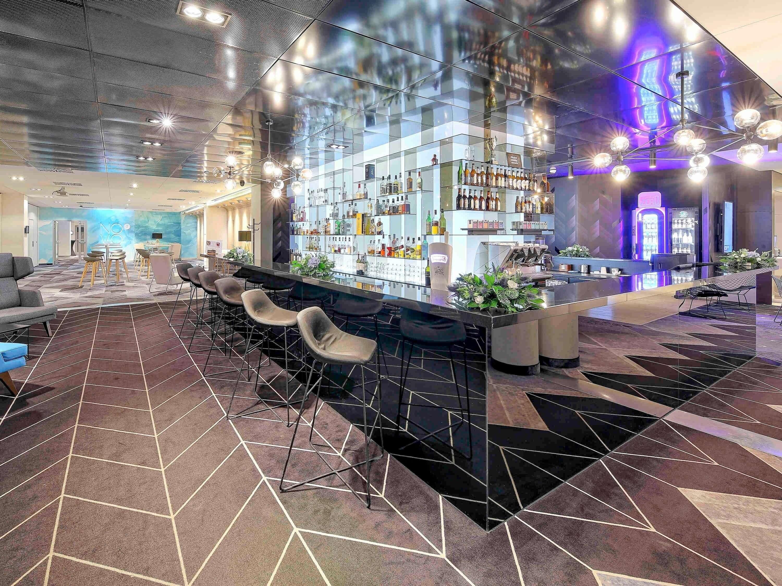 A modern bar area with a long counter, multiple stools, and a variety of bottles.