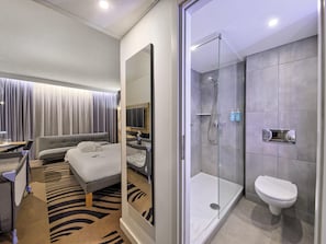 Une chambre d’hôtel moderne équipée d’un lit, d’une douche, de toilettes et d’un grand miroir.