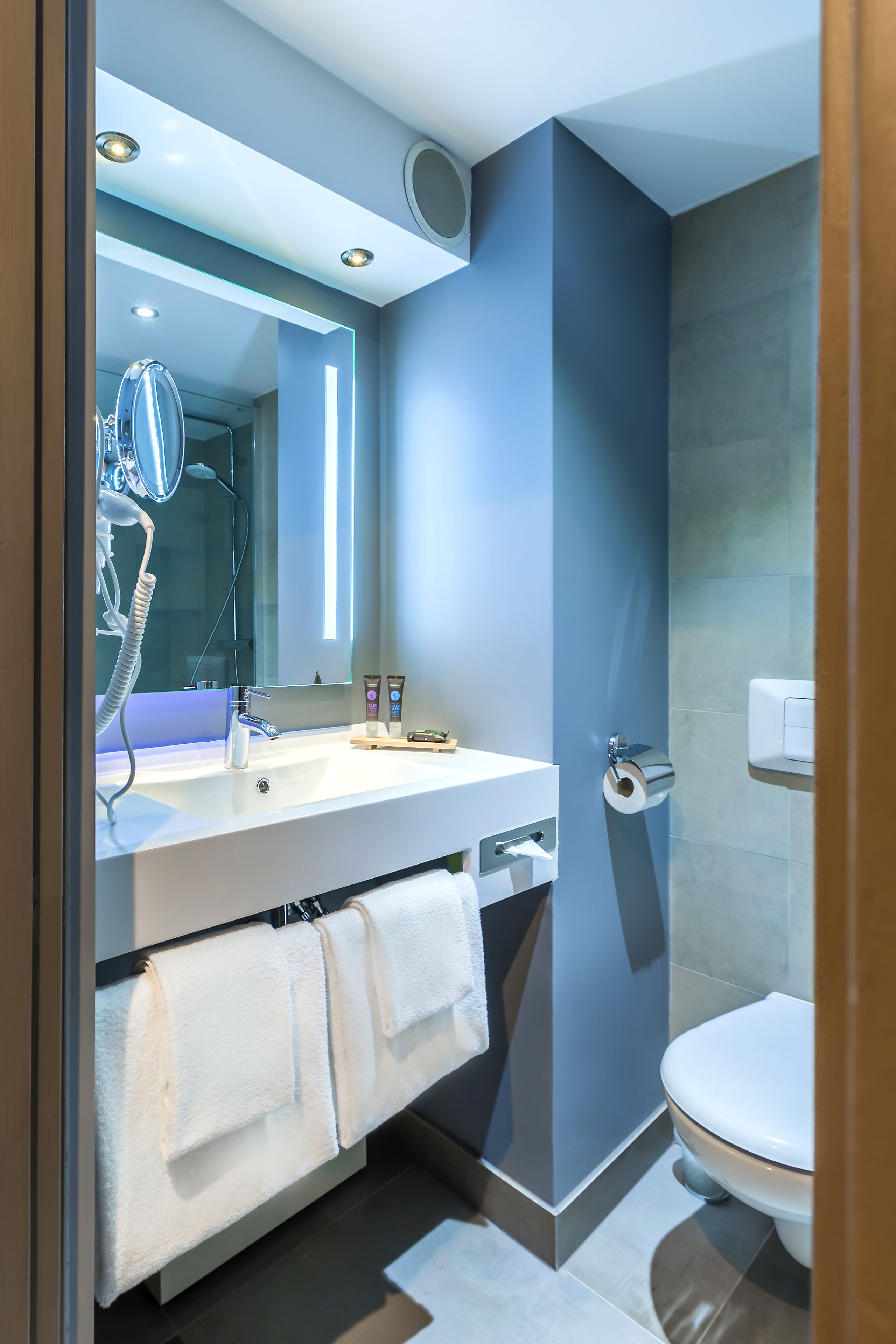 Un baño moderno con un espejo grande, un lavabo blanco, un inodoro y un perchero para toallas.