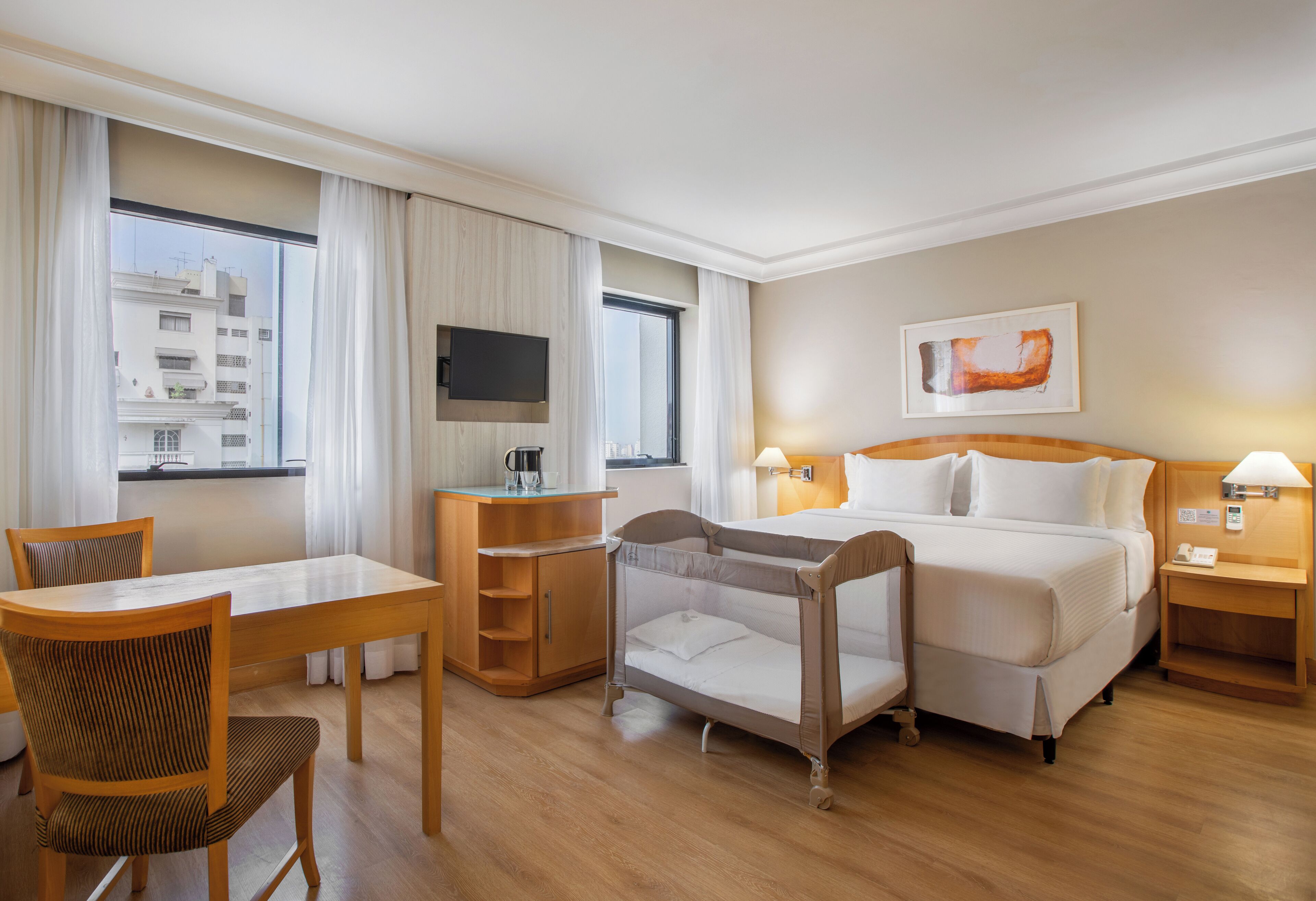 Une chambre d’hôtel avec un lit, un bureau, une chaise, une petite table, une télévision et une fenêtre avec des rideaux.