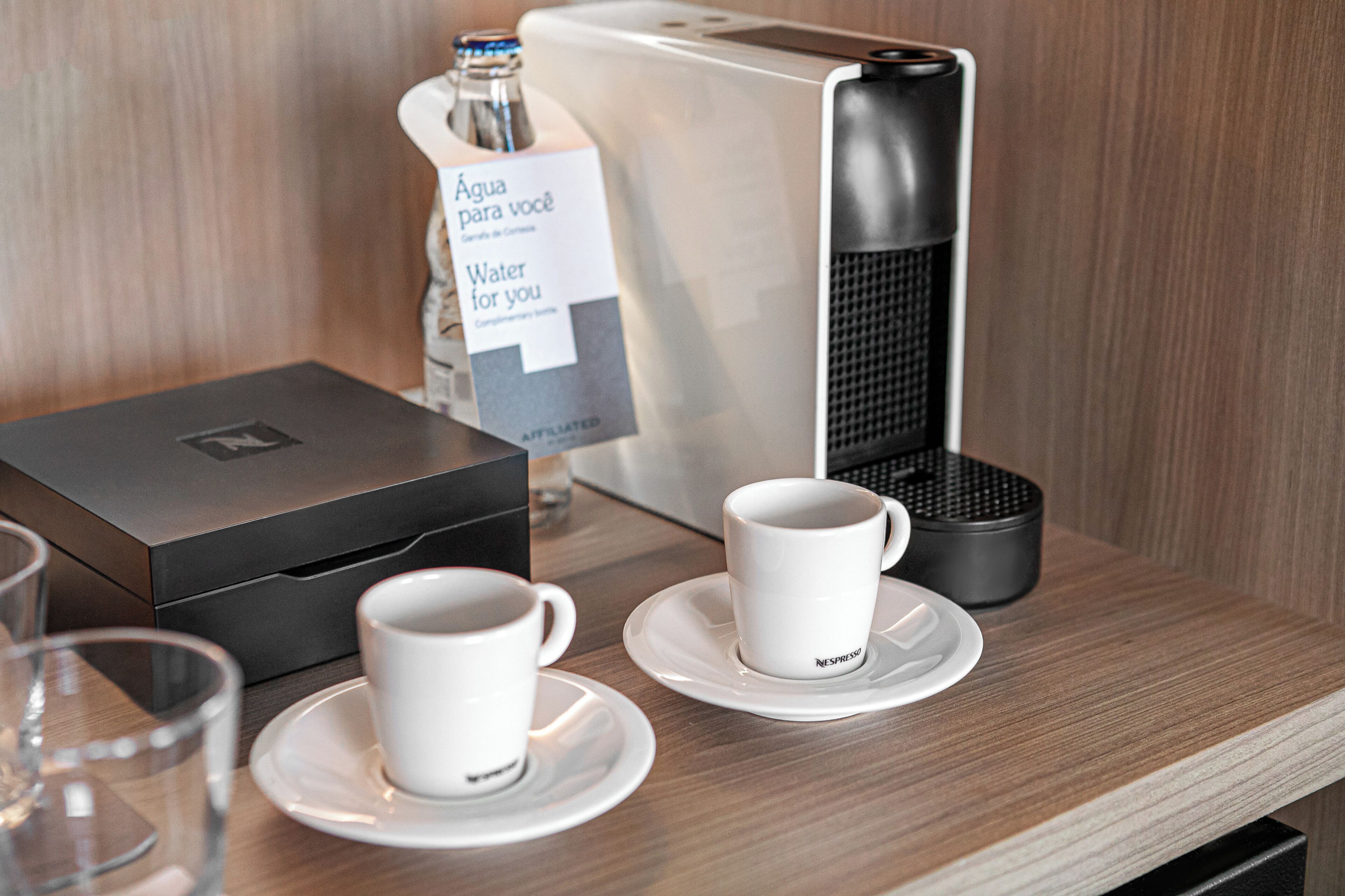 A coffee machine, a water bottle, and two white cups on a wooden table.