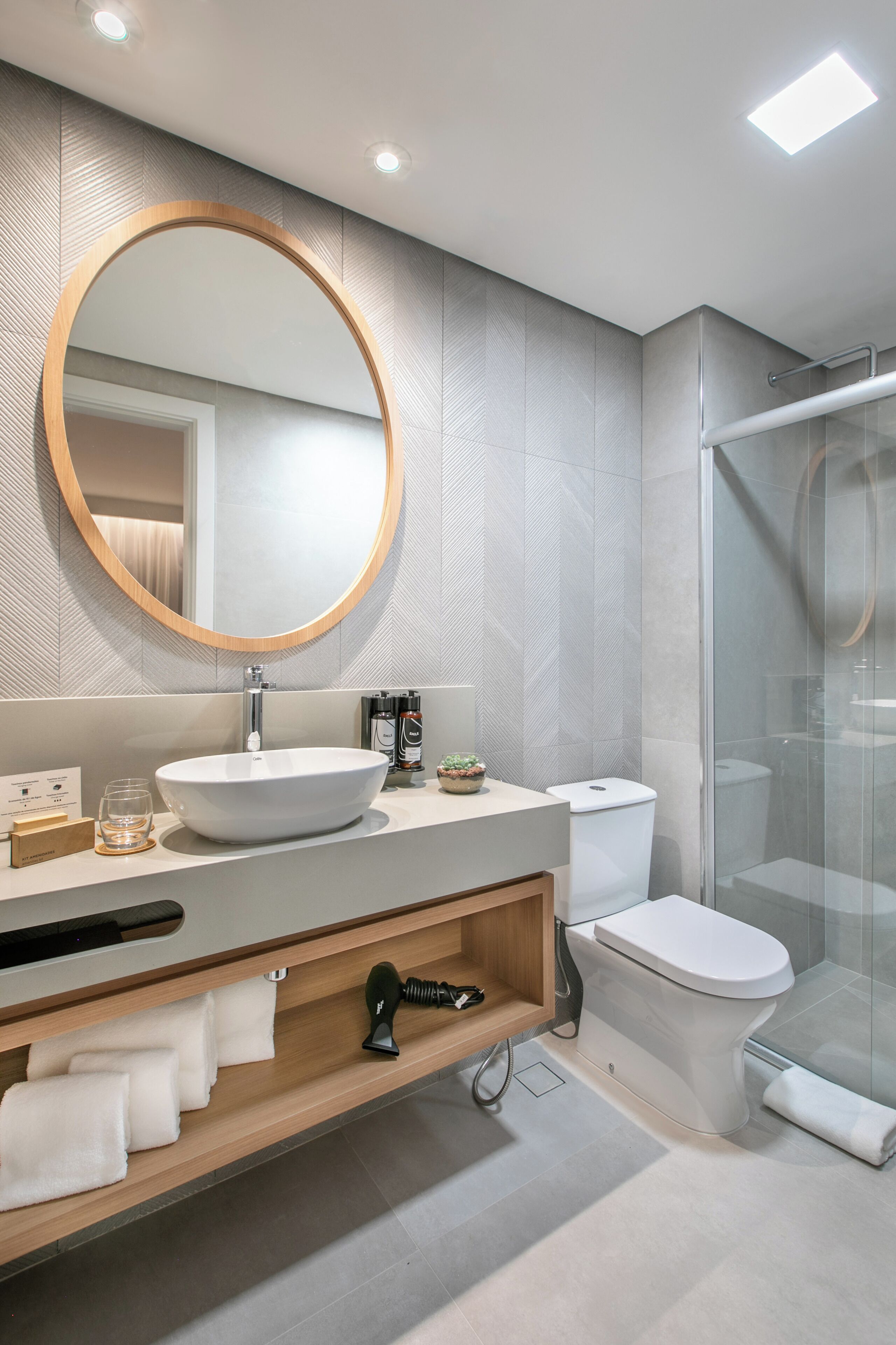 Un baño moderno con espejo redondo, lavamanos blanco y cabina de ducha de vidrio.