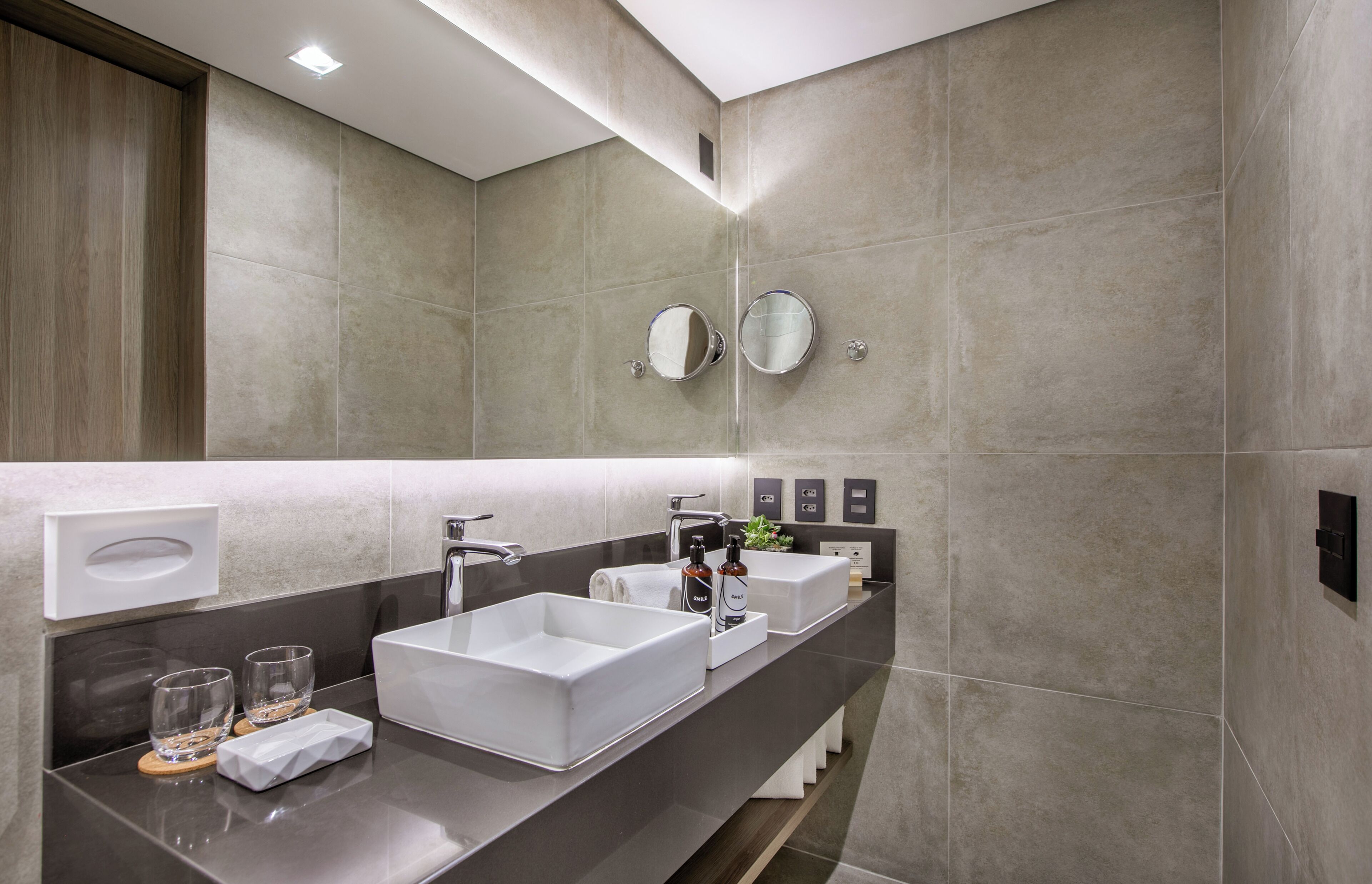 A modern bathroom with two white sinks, a large mirror, and a dark countertop.