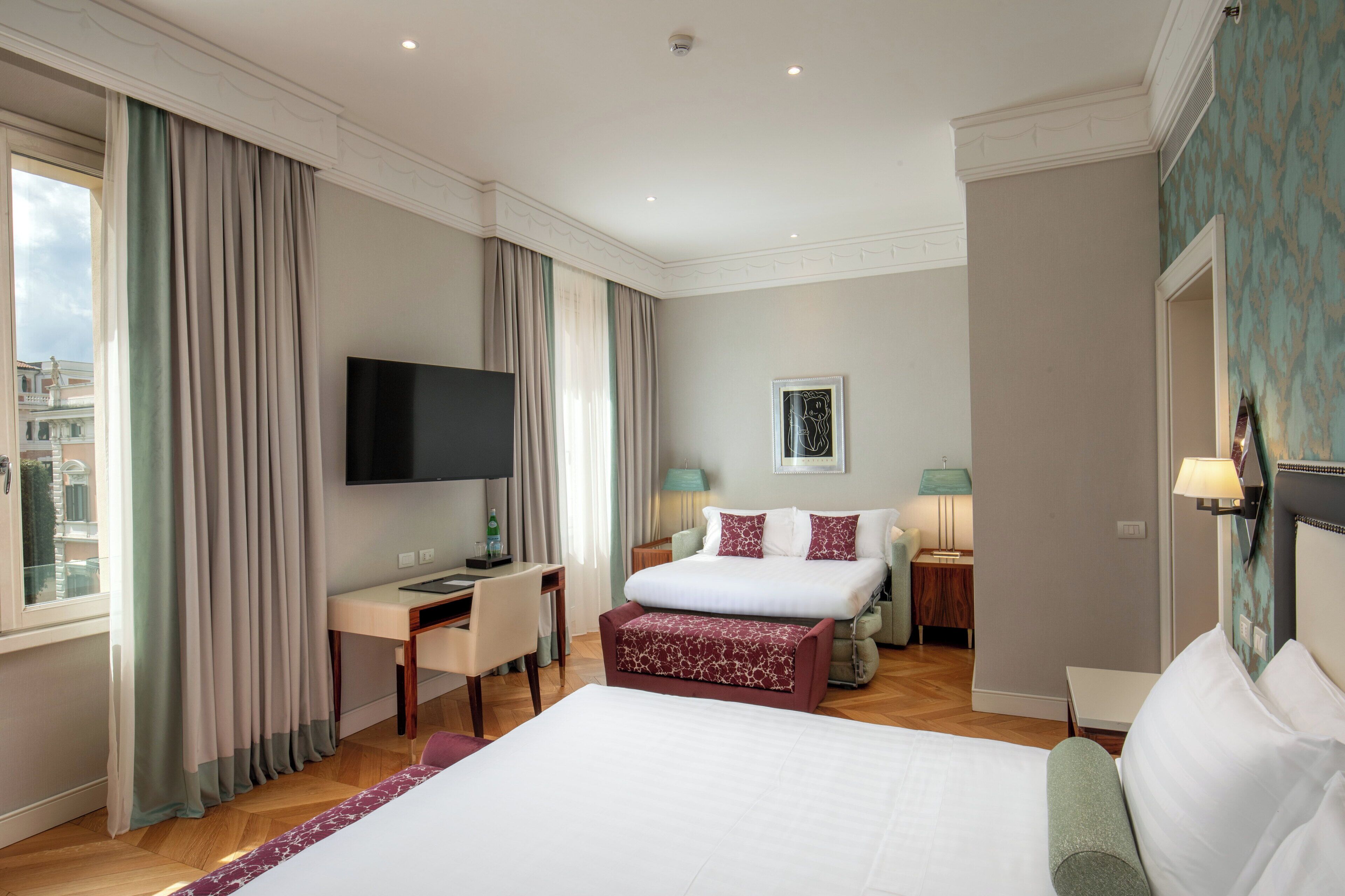 A hotel room with a large bed, a desk, a television, and a view of the city.