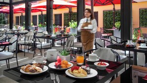Un restaurante con terraza, mesas con sombrillas y un camarero sirviendo comida.