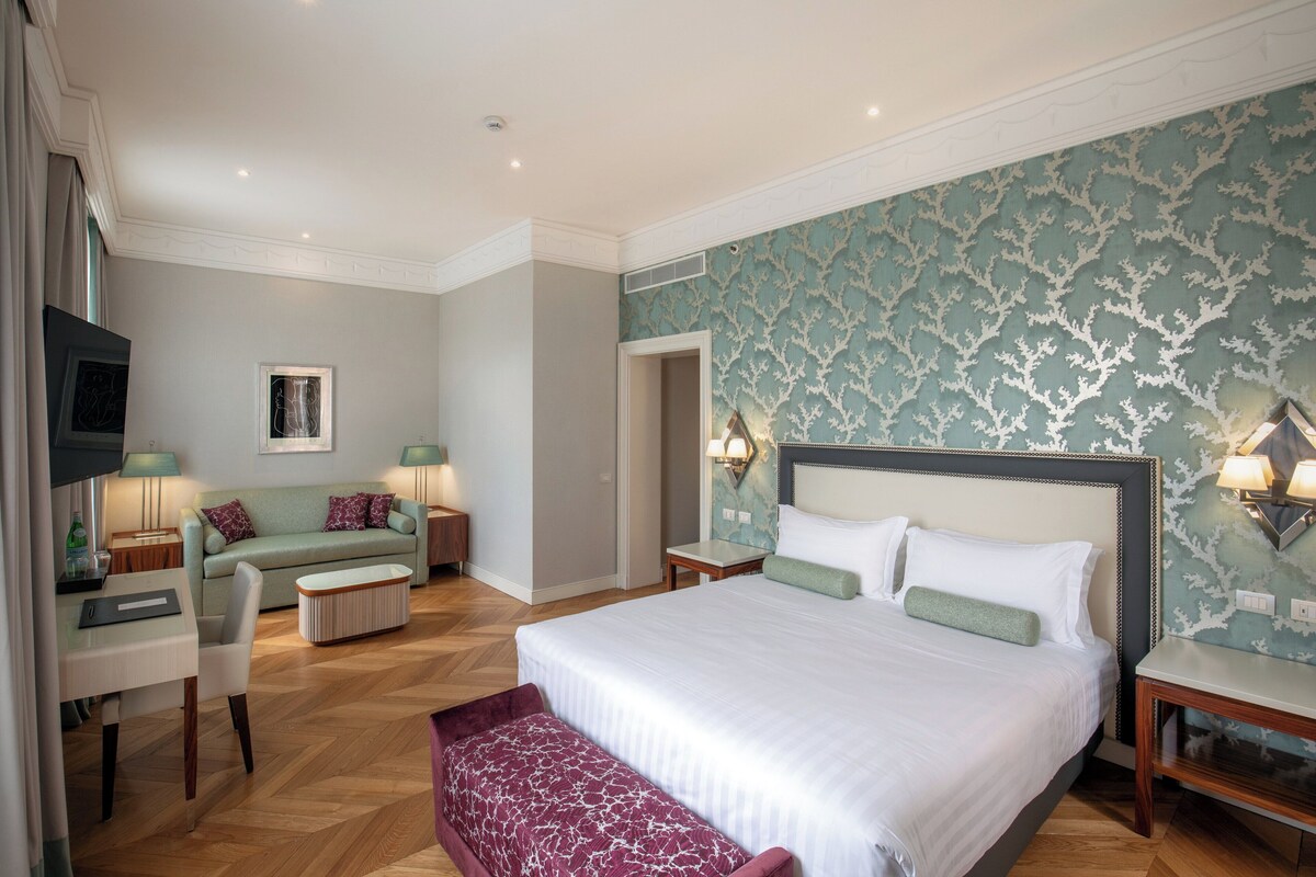 A hotel room with a large bed, a sofa, a desk, and a bench.