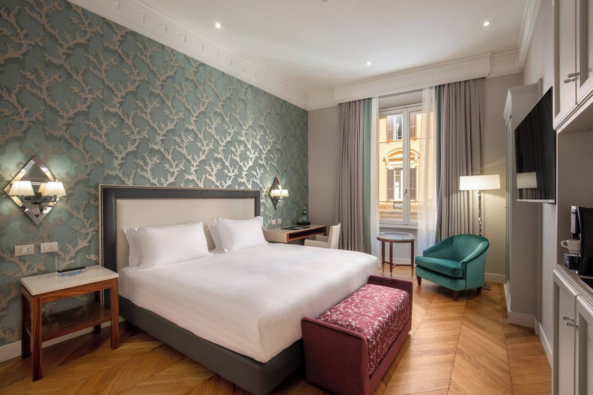 A hotel room with a large bed, a desk, a chair, and a television.