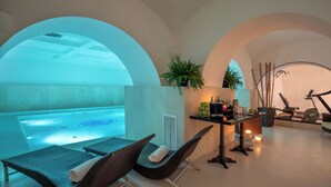 Un área de spa con un jacuzzi, dos sillones de mimbre, una mesa con velas y una planta en la pared.