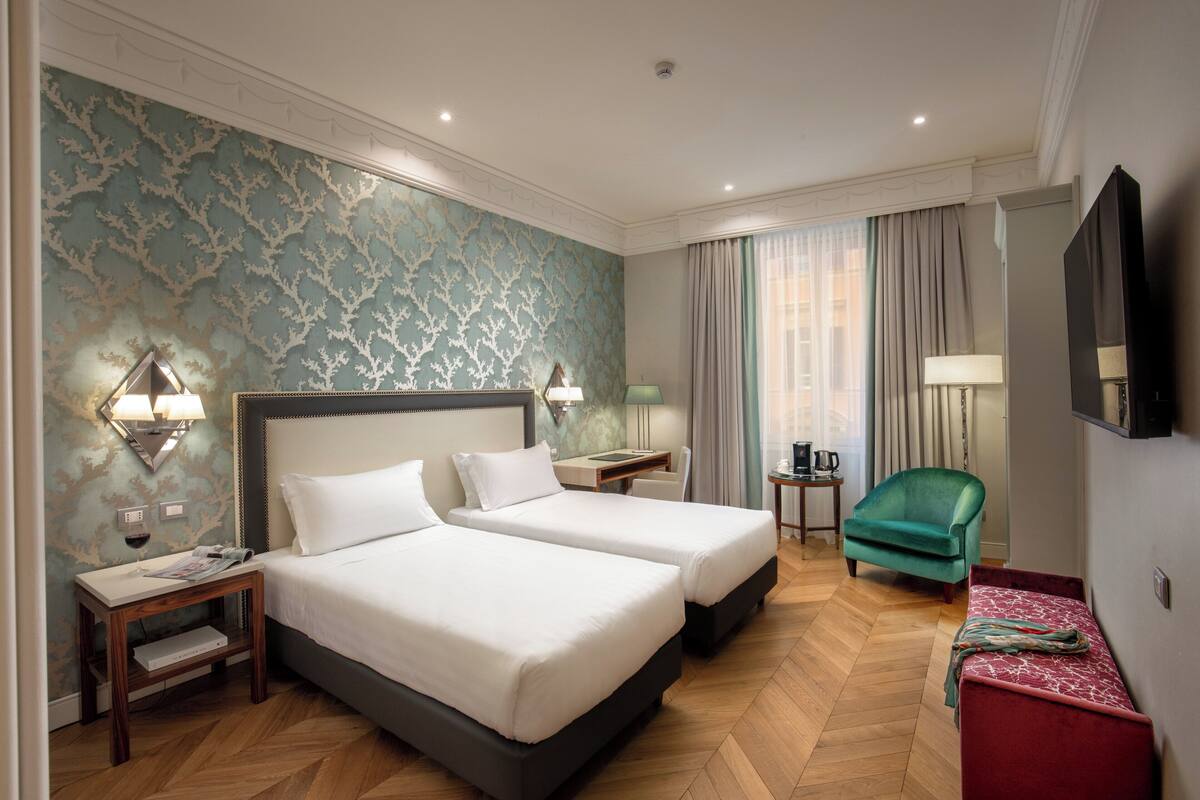 A hotel room with two beds, a desk, a chair, and a TV.