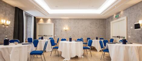 A conference room with round tables, blue chairs, and white tablecloths.