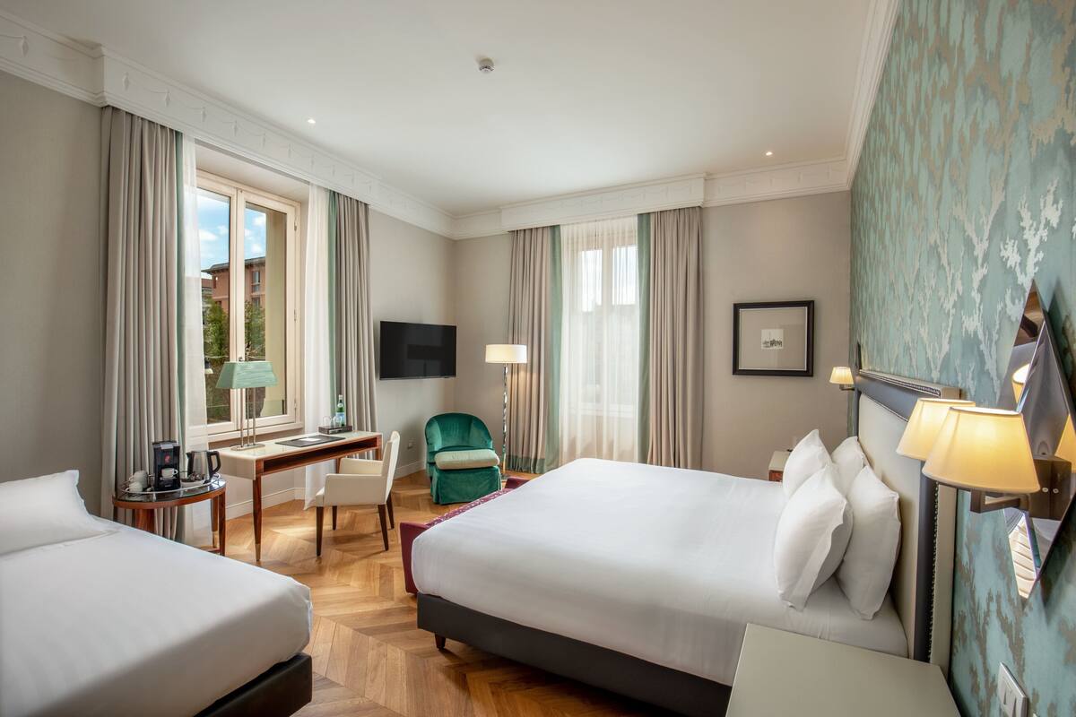 A hotel room with two beds, a desk, a chair, a TV, and a window with curtains.