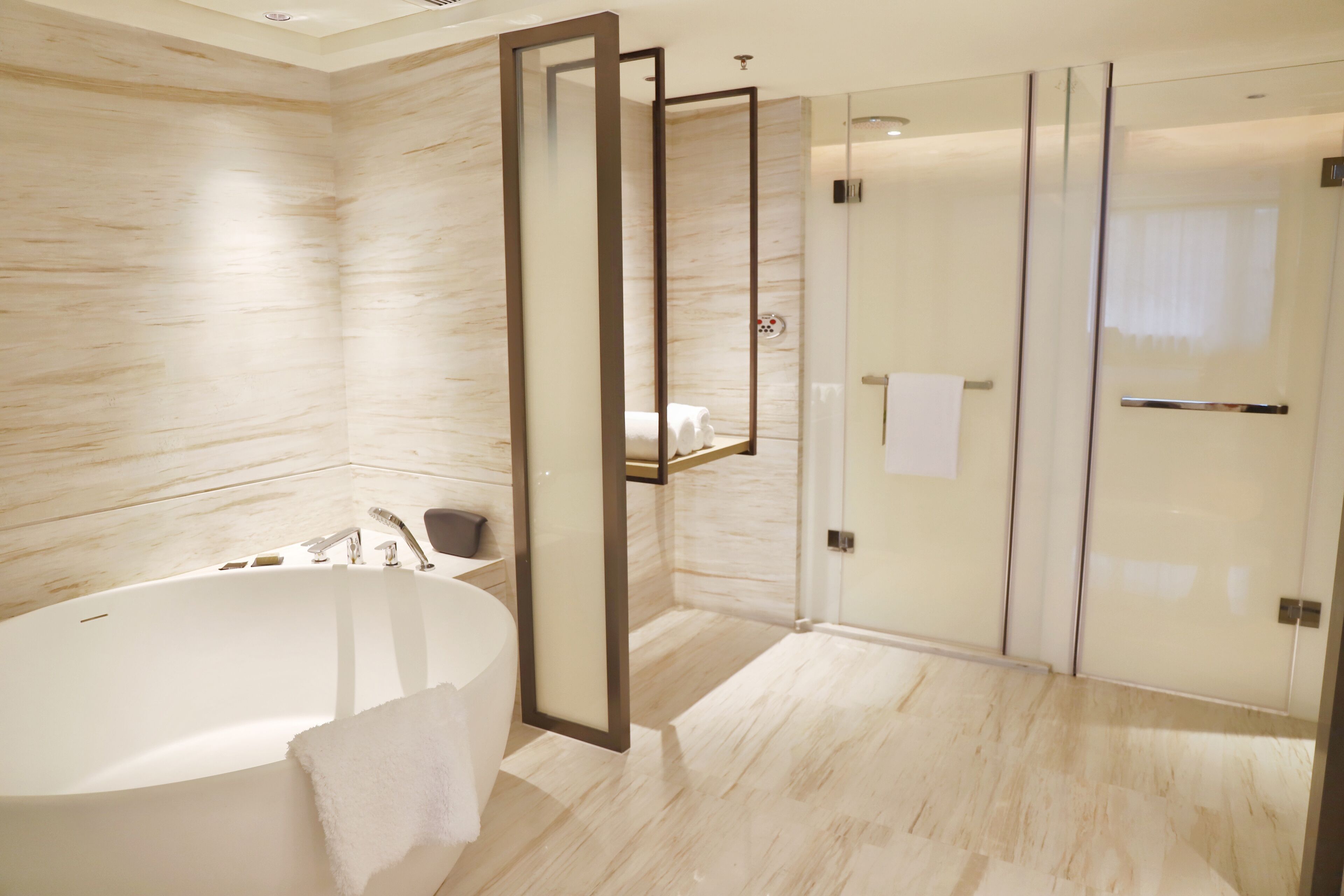 Un baño moderno con una bañera independiente, una ducha con mampara de vidrio y suelo de mármol.