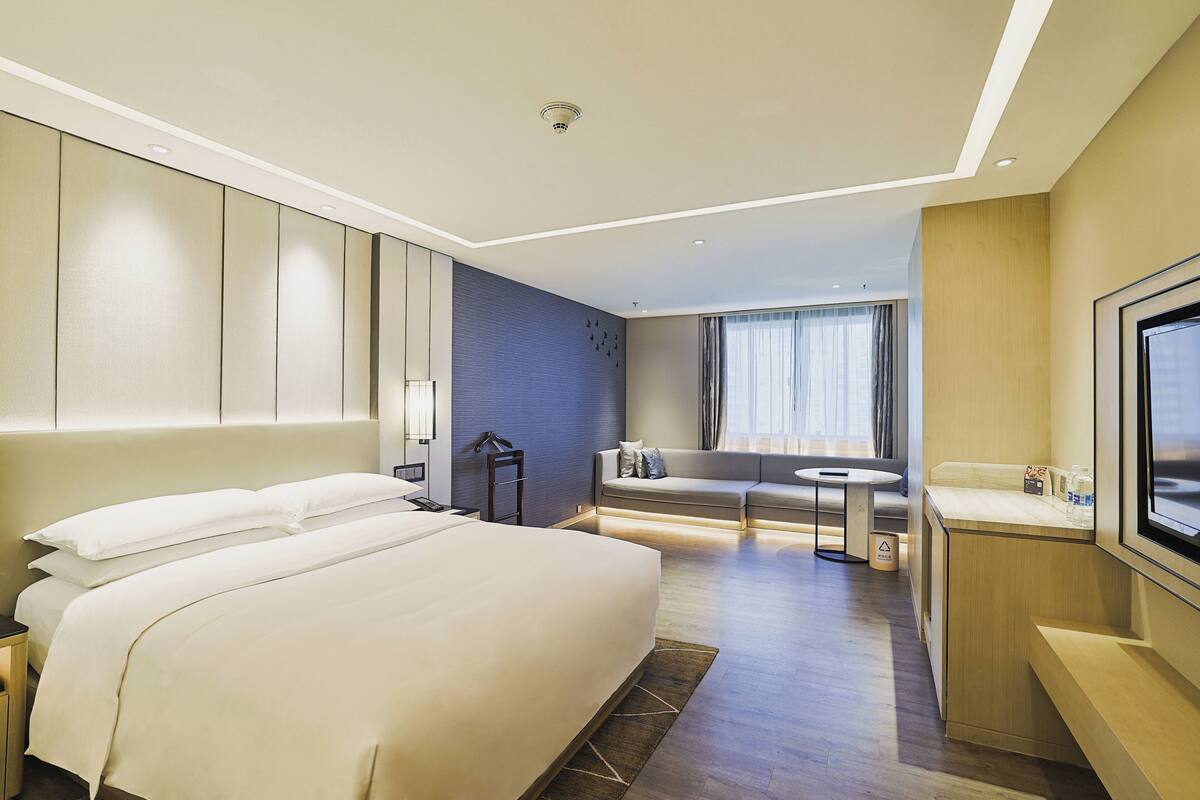 A hotel room with a large bed, a seating area, a TV, and a small table.