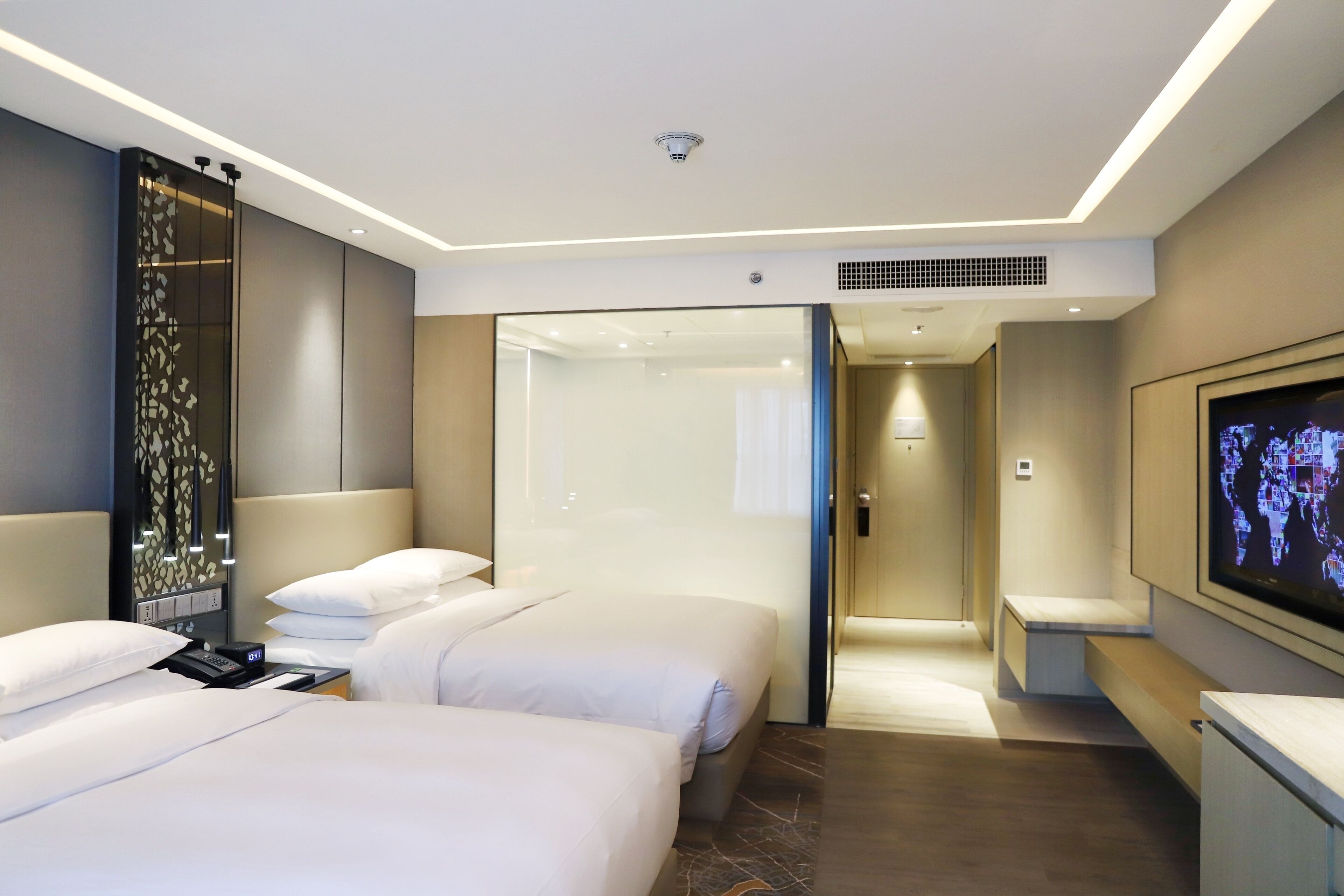 Une chambre d’hôtel avec deux lits, une télévision, un bureau et une salle de bain visible à travers une porte en verre.