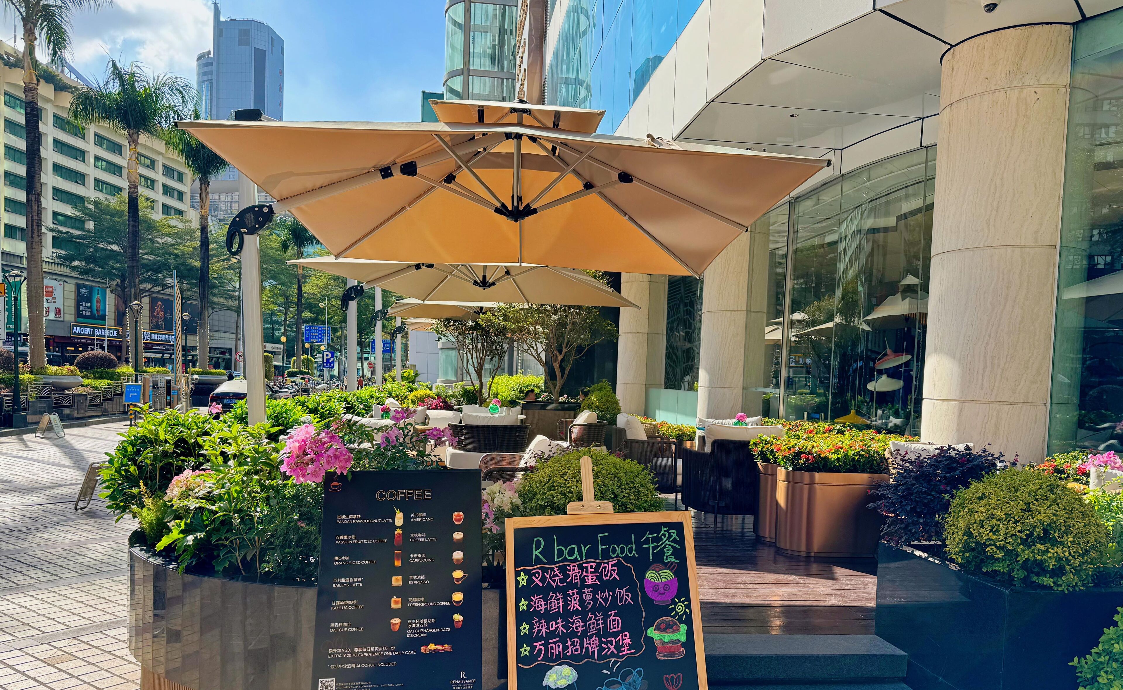 Un espace extérieur aménagé avec des parasols, un panneau affichant le menu et des plantes en pot.