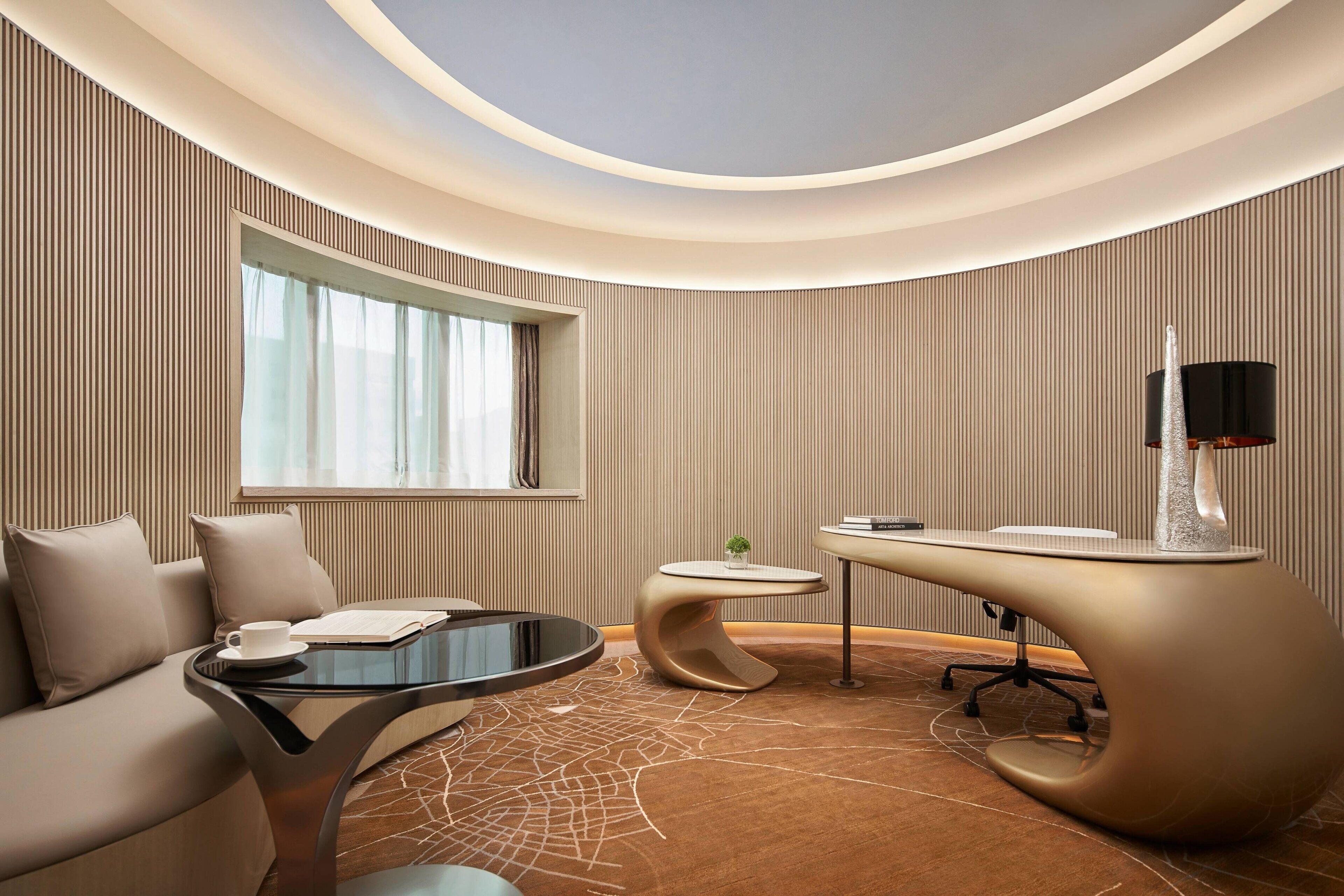 A modern hotel room with a curved ceiling, a round glass table, a sofa, a small round table, and a unique lamp.