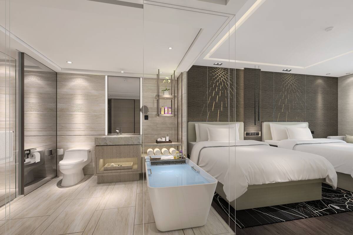 A modern hotel room with a large bed, a separate shower area, a vanity with a mirror, and a seating area with a table.