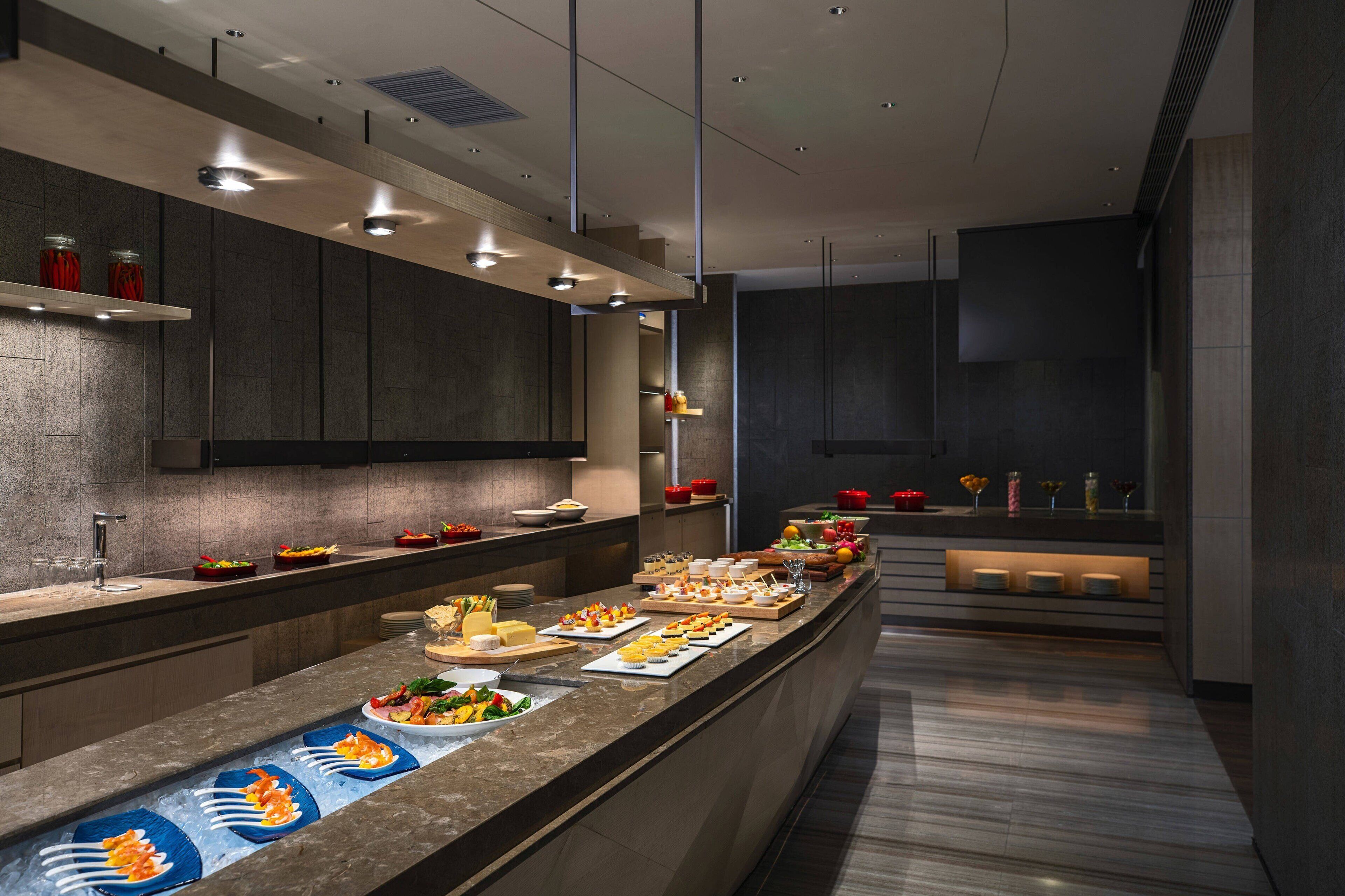 A modern kitchen with a long counter displaying various food items and a built-in refrigerator.