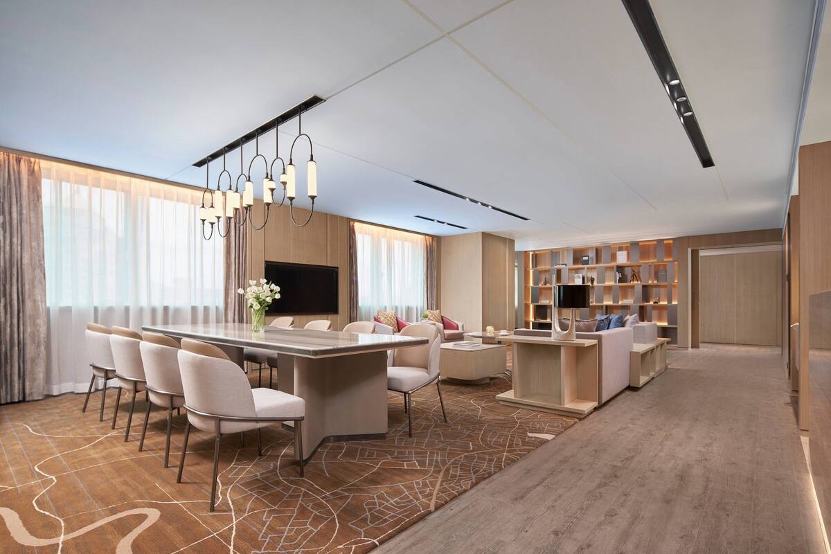 A modern hotel room with a dining area, a living area with a sofa and TV, and a bookshelf.