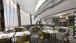Un restaurante moderno con mesas redondas, sillas verdes y un área de cocina visible a través de un separador de vidrio.