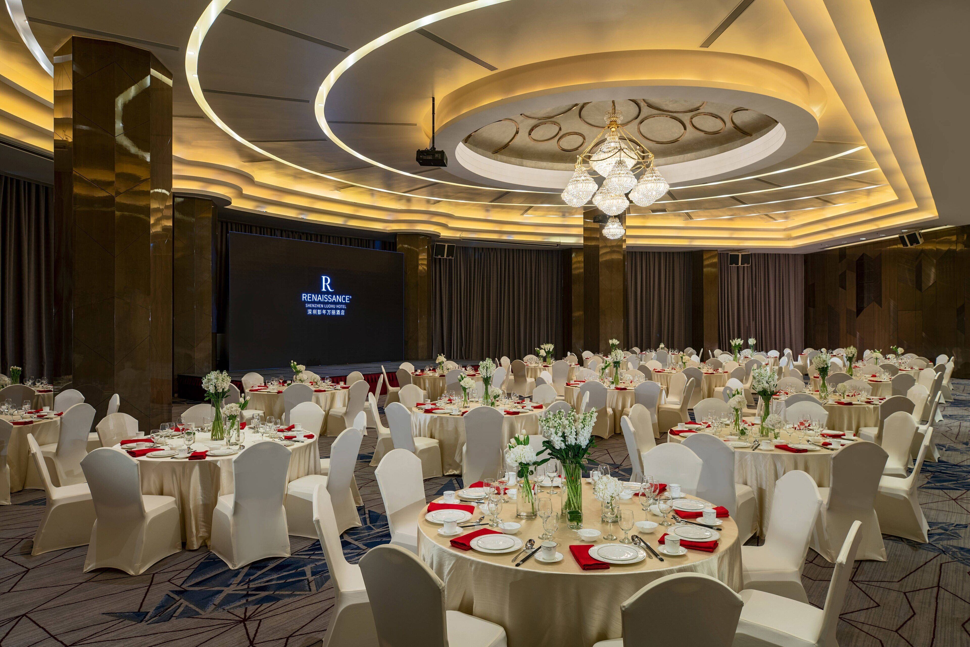 A banquet hall with round tables, white chairs, and floral centerpieces.