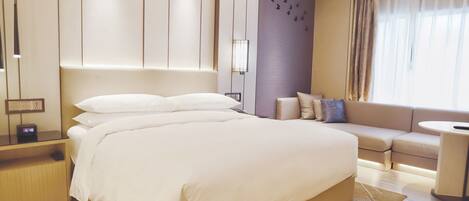 A modern hotel room with a large bed, a sofa, a small table, and a nightstand with a clock.