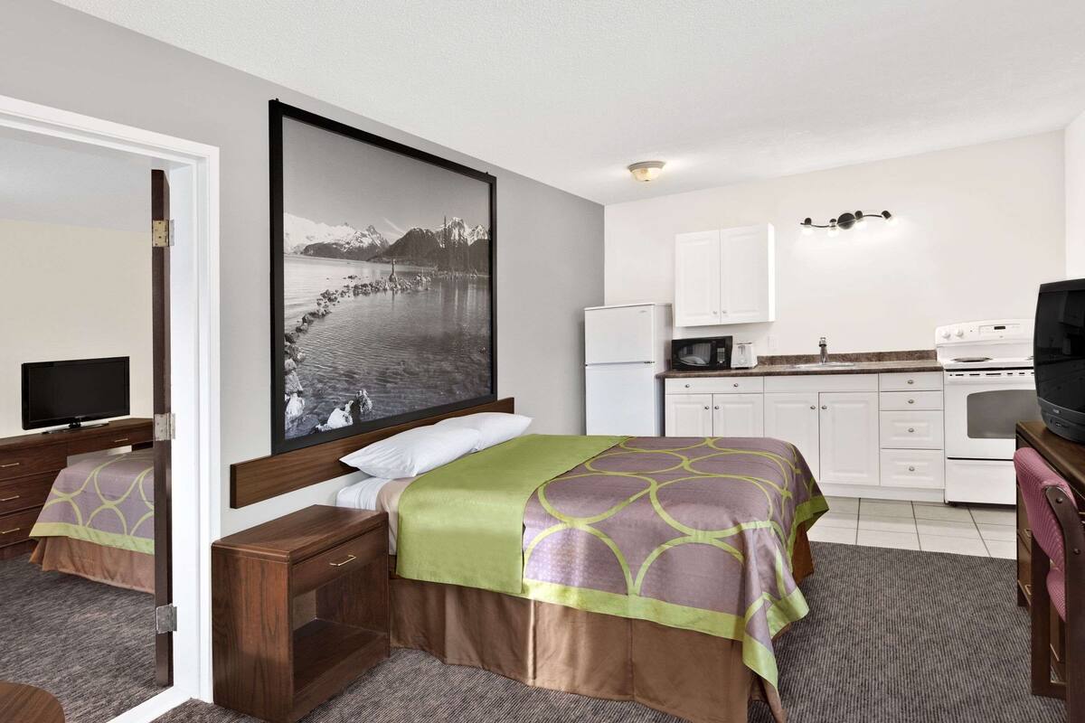 Une chambre d’hôtel comprenant un lit, un bureau avec un ordinateur, une télévision et un coin cuisine équipé d’un réfrigérateur, d’un four à micro-ondes et d’une cuisinière.